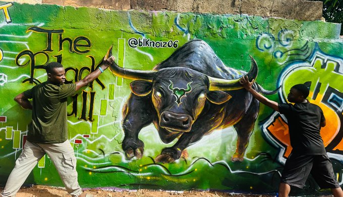 Two men posing playfully in front of a vibrant green graffiti mural featuring a charging bull and the text 'The Bull' and '@blknoiz06'.