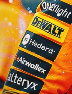 Close-up photo of brand stickers on an orange surface, including Oneflight, DeWalt, Hederδ, Airwallex, and Alteryx.