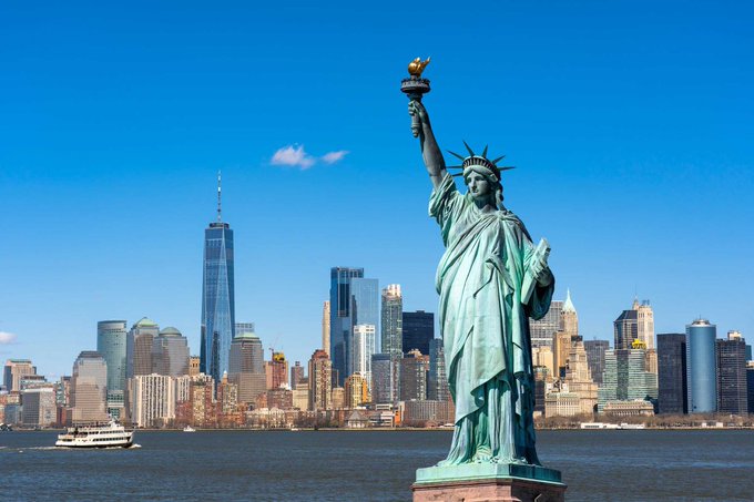 The Statue of Liberty stands prominently in the foreground against the backdrop of the Lower Manhattan skyline, including One World Trade Center, with the image symbolizing New York's role as the backdrop for news that the $295 billion New York State Retirement Fund has trimmed its $MSTR holdings by 11,400 shares while retaining Bitcoin exposure for 1.2 million employees.