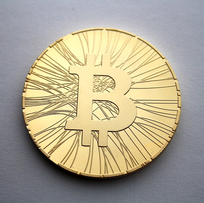 A golden Bitcoin coin featuring the iconic 'B' symbol rests on a light gray surface.
