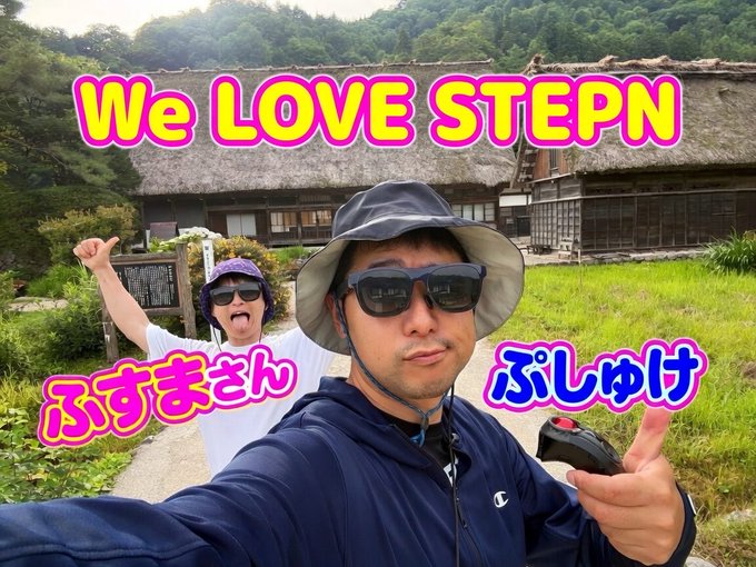A selfie of two people in front of a traditional Japanese thatched-roof house with the overlay text 'We LOVE STEPN' and Japanese labels 'ふすまさん' and 'ぶしゅけ' identifying each person.