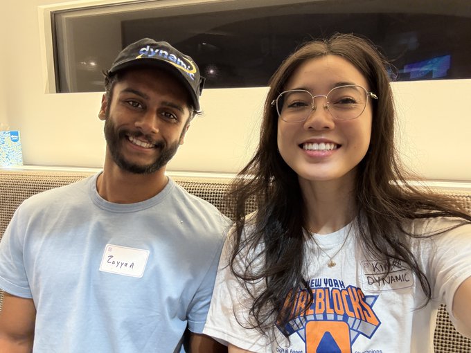 A selfie of two smiling people wearing name tags 'Zayyad' and 'Kim', with the man wearing a 'dynamic' cap and the woman wearing a New York Knicks 'Kid Blocks' shirt and glasses.