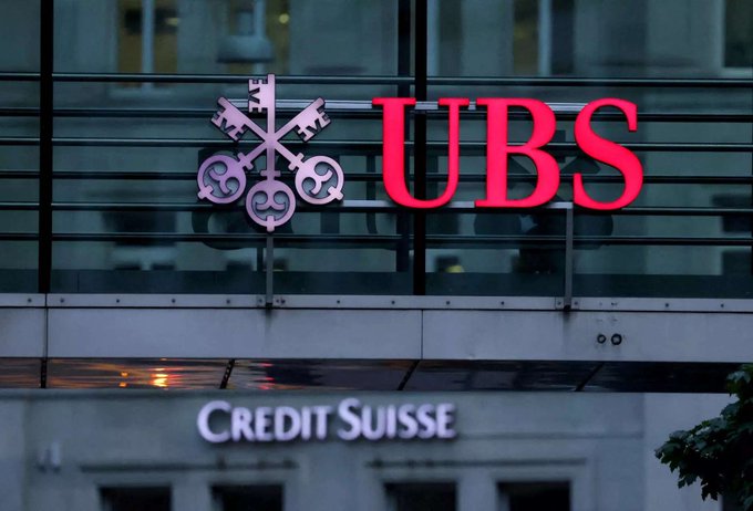 The image shows a UBS bank sign prominently displayed in red lettering with its distinctive key logo above a "Credit Suisse" sign, illustrating UBS's significant financial moves—including its $83.2M Bitcoin ETF investment—even as retail investors remain fearful of further price declines.