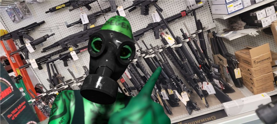 A green zombie character wearing a gas mask stands in front of a wall displaying numerous firearms at a gun store, pointing at the weapons.