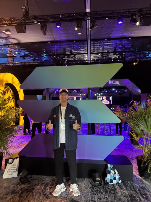 A man gives two thumbs up in front of a large Solana logo sculpture at what appears to be a conference, with a 'Token2049' sign visible in the background.