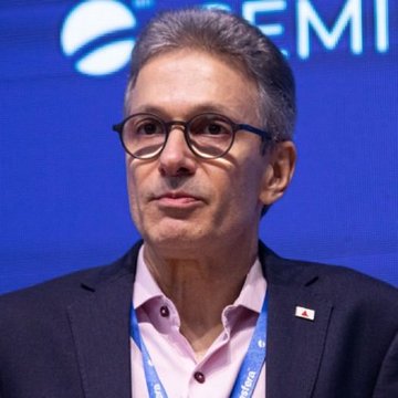 A man with glasses wearing a dark blazer over a pink shirt stands at what appears to be an SEMI conference event.