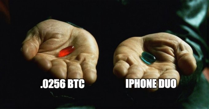 The image is a parody of the iconic "red pill, blue pill" scene from The Matrix, showing two hands holding pills labeled ".0256 BTC" (red pill) and "IPHONE DUO" (blue pill). The meme humorously frames a choice between a fractional amount of Bitcoin and an iPhone Duo as a Morpheus-style decision, fitting the post's sentiment that someone is "beginning to believe" in Bitcoin over traditional consumer tech purchases.