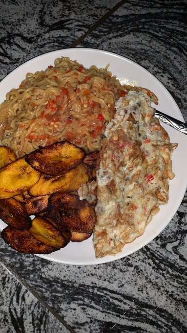 A plate of food featuring noodles with red sauce, fried plantains, and an omelet on a marbled surface.
