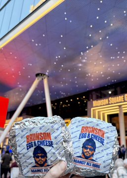 Two packages labeled "Bruinsons Egg & Cheese" are held up in front of a stadium marquee.