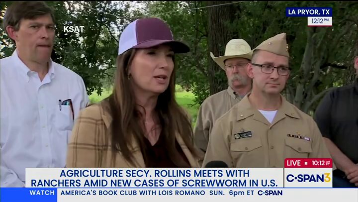 The image shows a news segment featuring two men wearing cowboy hats and military uniforms standing next to each other. The first man has his arm around the second man's shoulder, while they both appear to be engaged in conversation or listening to something on a television screen.