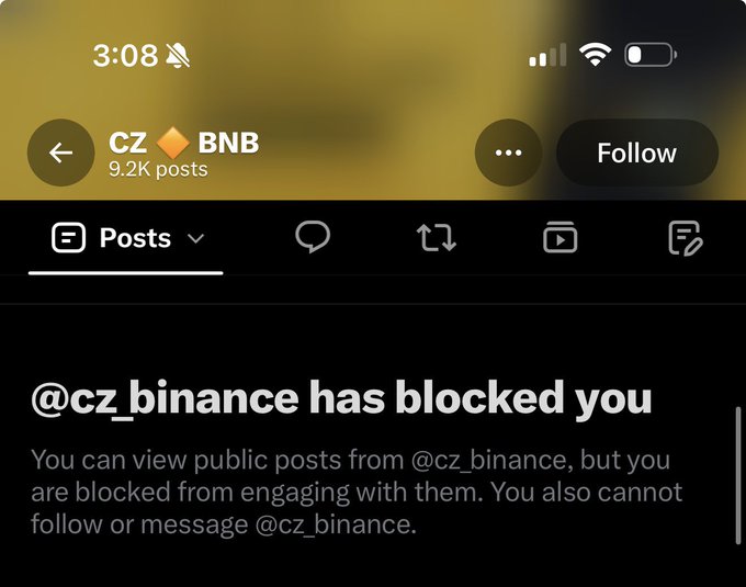 A mobile screenshot shows the X profile of CZ BNB (@cz_binance), which has 9.2K posts, displaying a notice that "@cz_binance has blocked you," preventing engagement despite public posts still being viewable—humorously illustrating the accompanying post's claim of being blocked by the Binance founder.