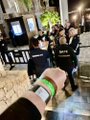 The image shows a group of people standing together, with one person holding up their wrist displaying a green bracelet. The background includes a building and a tree, suggesting an urban setting. The caption reads "Otherside IRLs VIPs only Exclusive mini Ape fest feel with @BoredApeYC family What else..) @mfigge said “it's coming..) Apecoin fam are die hard connections) Memories forever & just a call away) @LadyMeme12345 @achimh @drdavecoin @novocrypto @Pausrr".