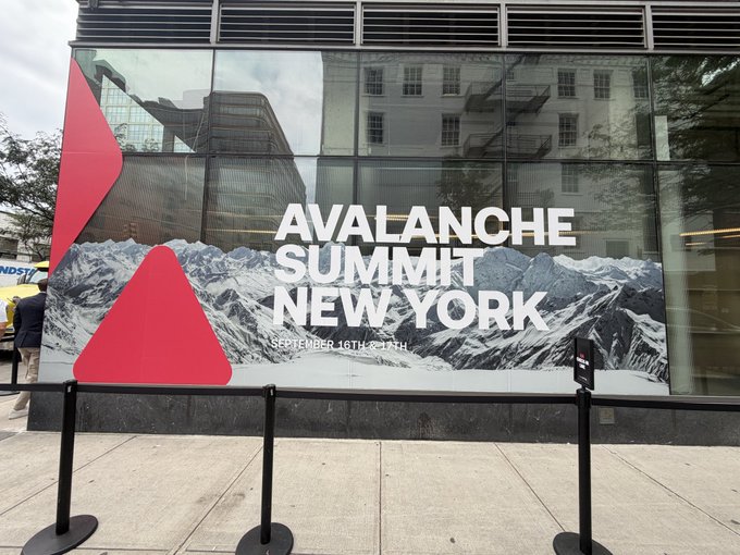 An outdoor banner on a city building reads 'AVALANCHE SUMMIT NEW YORK, SEPTEMBER 16TH - 17TH' against a snowy mountain backdrop.