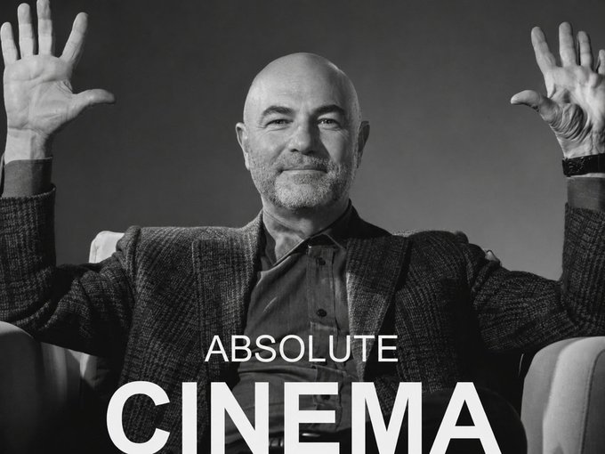 A black and white portrait of a bald, bearded man with both hands raised, wearing a blazer and shirt, with the text 'ABSOLUTE CINEMA' overlaid at the bottom.