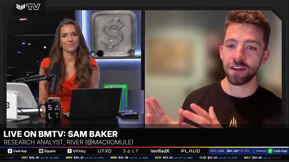 A live BM TV broadcast featuring a woman in an orange top in a studio and a man on a split-screen; the banner reads 'LIVE ON BMTV: SAM BAKER, RESEARCH ANALYST, RIVER (@MACROMULE)' with a BTC/USD price of $86,260 shown at the bottom.