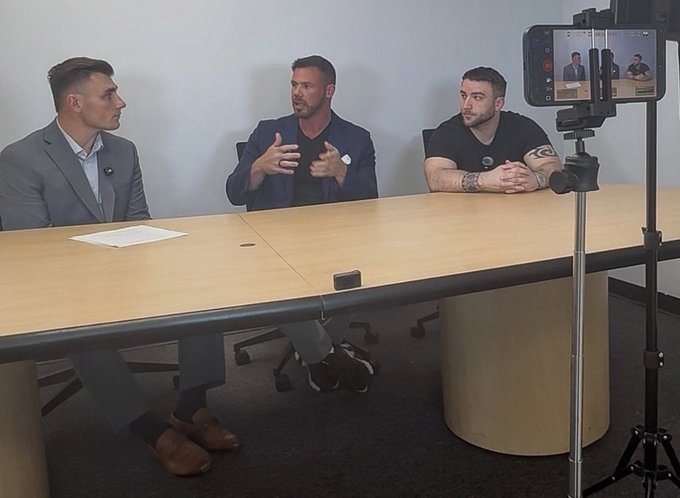 Three men are seated at a conference table being recorded by a smartphone on a tripod, with the central figure in a blue blazer gesturing while speaking, appearing to be the "Jake Claver" referenced in the post as an XRP commentator. The setup captures an in-person interview or podcast recording, supporting the claim of a real-world meeting.
