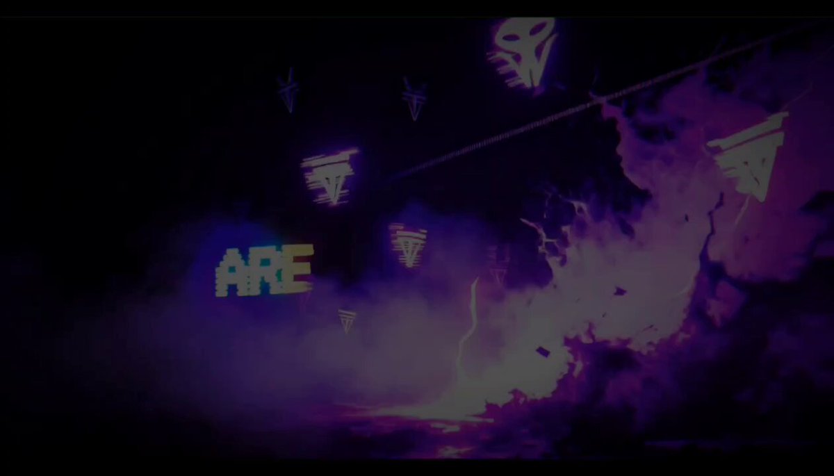 The image features a large purple screen with the words "ARE" written on it, surrounded by neon lights that create an atmospheric effect. The background of the image shows a dark sky filled with smoke coming from a firework display. The combination of these elements creates a visually striking scene and suggests that there might be something exciting or unexpected happening inside the arena.