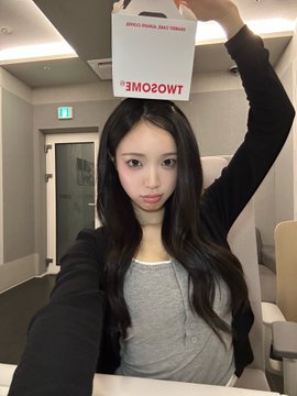 A young woman with long black hair holds a TWOSOME PLACE paper bag upside down over her head while taking a selfie indoors.