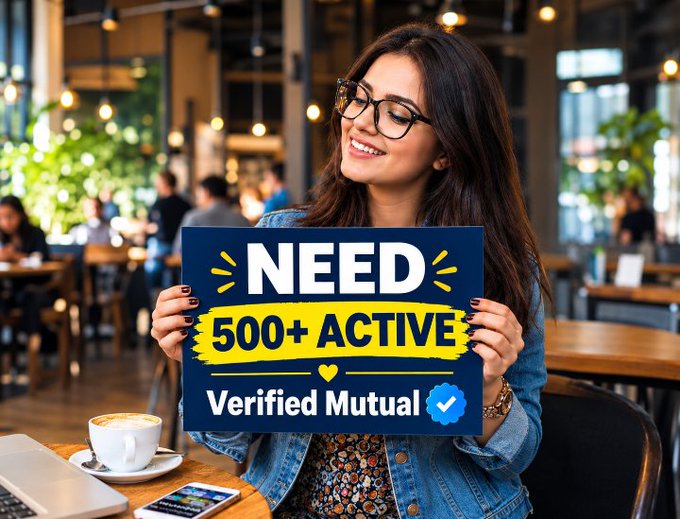 A smiling woman with glasses holding a blue and yellow sign that reads 'NEED 500+ ACTIVE Verified Mutual' with a checkmark, seated at a cafe table.
