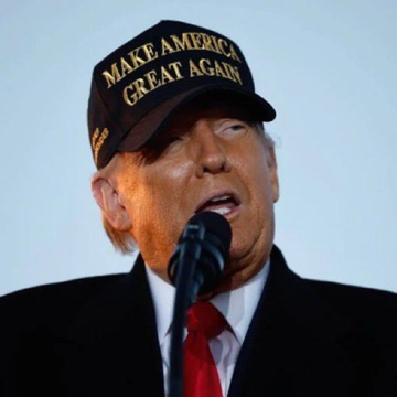 Former U.S. President Donald Trump speaks into a microphone while wearing a black 'MAKE AMERICA GREAT AGAIN' baseball cap.