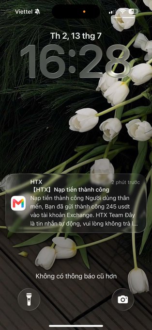 A smartphone lock screen with a white tulip wallpaper displays a Vietnamese notification from the HTX exchange about a successful deposit of 245 USDT, with the time shown as 16:28 on Thursday, July 13th.