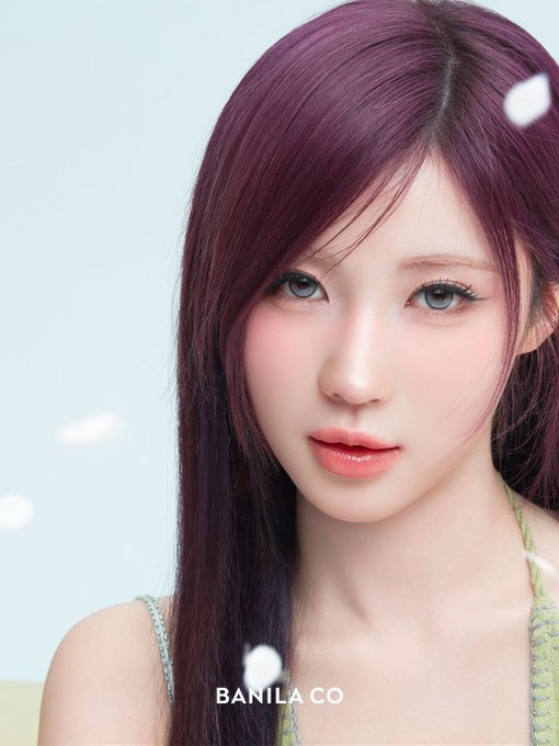 A close-up beauty portrait of a woman with long magenta hair and grey contact lenses, branded with the 'BANILA CO' logo at the bottom.