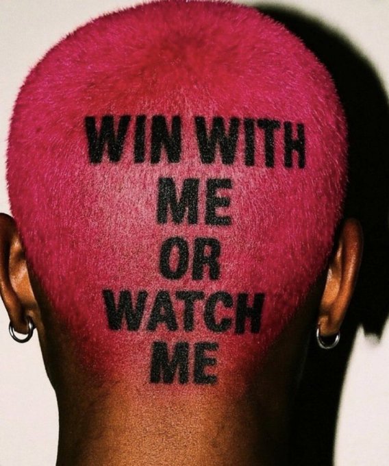 The back of a person's head with pink-dyed hair and a shaved undercut, featuring the text 'WIN WITH ME OR WATCH ME' printed in black on the shaved portion.