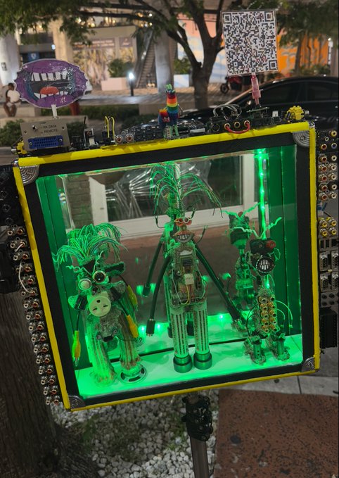 A yellow-framed illuminated display case lit in green showcases three small robot figures with antennae, topped with a rainbow pinwheel and a QR code.