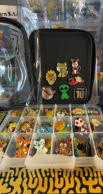 A collection of Disney and pop culture collectible pins displayed in a black zippered case and an organized clear plastic tray, featuring characters like Simba, Stitch, Ariel, and Dumbo.