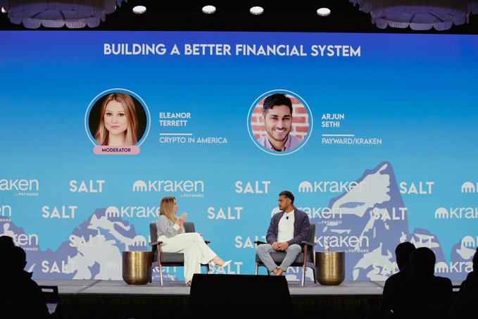 A moderator, Eleanor Terrett of Crypto in America, interviews Arjun Sethi of Payward/Kraken on stage under the banner "Building a Better Financial System," with Kraken and SALT logos displayed behind them. The image relates to the post by capturing a panel discussion from the Wyoming Blockchain Symposium, likely streamed for those unable to attend in person.