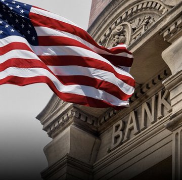 An American flag waves in front of a classical building marked "BANK," symbolizing the intersection of U.S. financial institutions and emerging policy discussions. The image visually reinforces the post's announcement about Congress considering legislative changes that would allow banks to engage in cryptocurrency and blockchain activities.