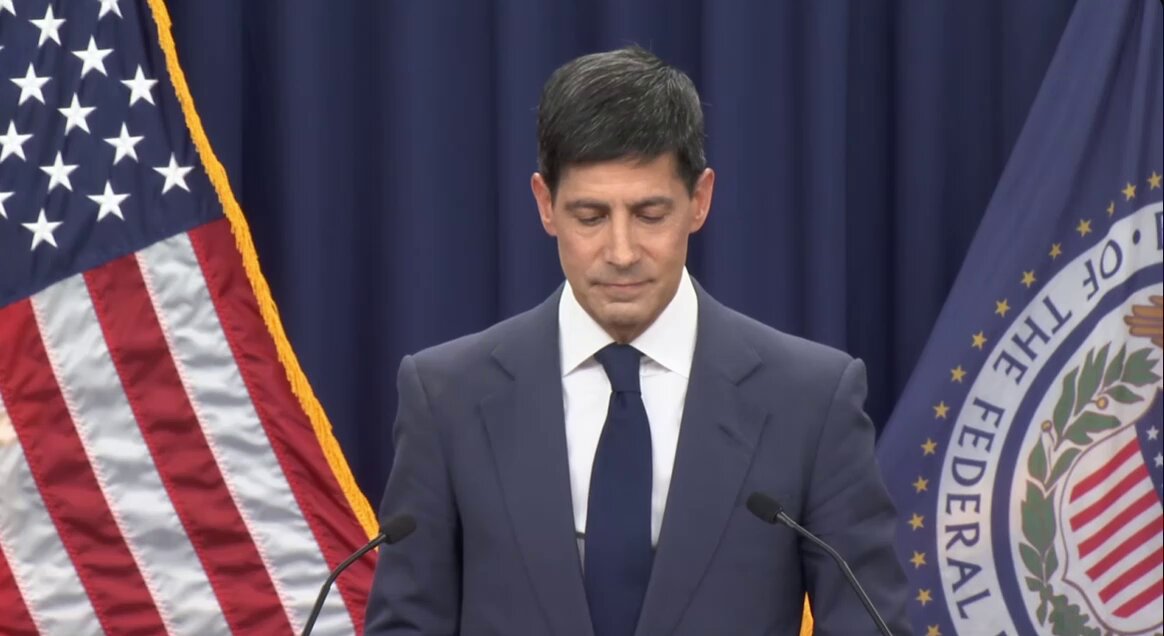 The image features a man standing at a podium, giving a speech or delivering a press conference. The man appears to be dressed in a suit and tie, suggesting that he holds an important position or has significant influence. Behind him, there are two flags - one representing the United States of America with its iconic stars and stripes design, and another flag symbolizing the Federal Reserve Bank of New York.

The post also mentions that the man is speaking at a press conference about the Fed Chair, which implies that he might be discussing economic matters or providing insights into the current state of the economy. The image captures this moment in time, with the focus on both the man and his surroundings.