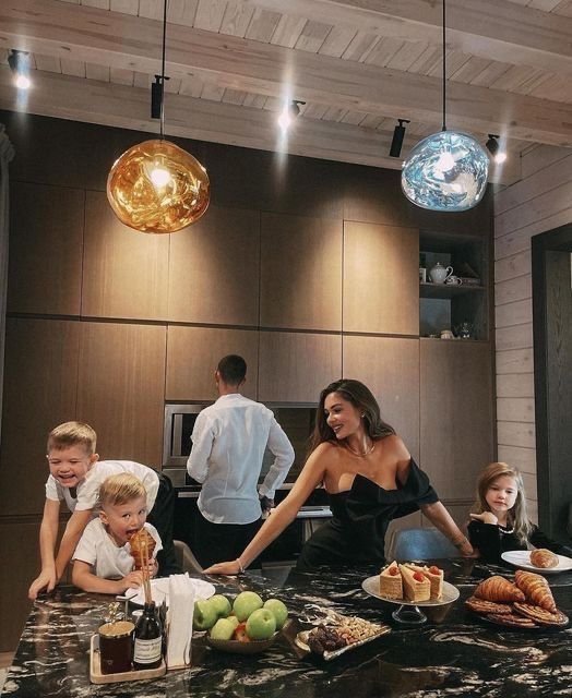 A family gathers around a luxurious black marble kitchen island filled with fresh pastries, fruit, and wine, while the mother smiles brightly as children lean in playfully. The post's joke about "$HBAR reaching $1" humorously contrasts the family's upscale, opulent lifestyle with the wild optimism of cryptocurrency holders imagining sudden wealth.