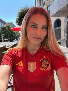 A woman wearing a red Spain national team jersey (with the Adidas logo and Spanish FA crest featuring one star) takes a selfie outdoors, visually tying into her prediction post about the Spain vs. Argentina final via OKX's World Cup Outcome Market.