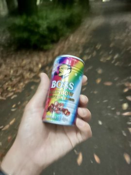 The image shows a person holding up a colorful can of soda, which appears to be a rainbow-colored drink. The text "BOSS" is visible on the can, indicating that this could be an advertisement for a fruity or sweetened beverage. The photo also includes a caption that reads "#STEPN".