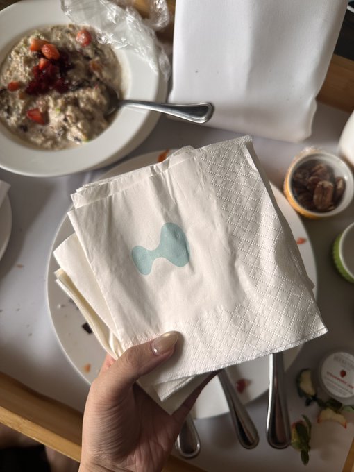 A hand holds a crumpled HYPE-branded napkin with its signature blue logo over a table with breakfast dishes, playfully illustrating the "1 tissue = 1 HYPE" compensation demand.