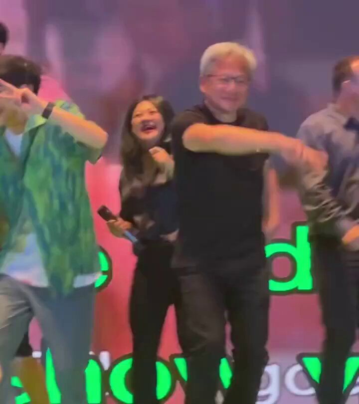 The image shows a group of people dancing together, with one man wearing glasses and holding a microphone while another woman stands next to him. The background features a large screen displaying the words "Telcoin hodlers in a couple of years $TEL".