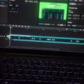 A close-up of a laptop screen shows a video editing software timeline and a small preview window displaying a green scene.