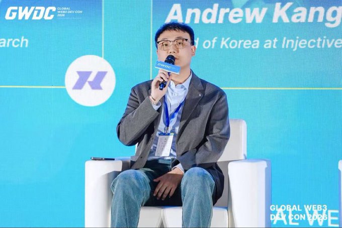 Andrew Kang, identified by the text behind him, speaks into a microphone at the Global Web3 Dev Con (GWDC) while seated on a white chair against a blue backdrop.