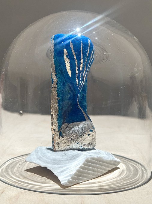 A blue and silver abstract sculpture displayed under a clear glass dome on a white base.