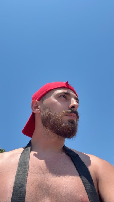 A bearded man wearing a red backwards cap and gray tank top gazes upward against a clear blue sky, capturing a fresh, optimistic morning vibe that pairs perfectly with the "Gm friends" greeting.