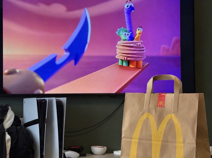 A McDonald's takeout bag sits in front of a TV displaying a scene from the animated show Claynosaurz, where colorful dinosaur characters are tied up with rope near a large knife, tying into the post about paying with a Solana debit card and watching the show on Amazon Prime.