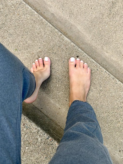 A first-person downward view of two bare feet with white painted toenails standing on concrete steps, with the left foot resting on a lower step.
