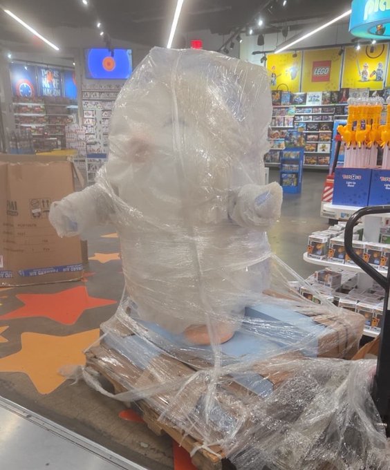 A store display features a plush polar bear figure entirely wrapped in clear plastic shrink wrap on a wooden pallet.