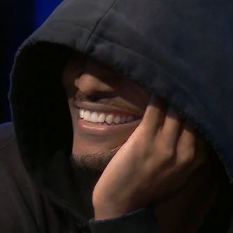 A hooded figure covers part of their face while smiling, with only their mouth, chin, and hand visible in the dim lighting. The image evokes the concealed, "masked dealer" persona, visually tying into the $DEALER meme coin concept introduced in the Ansem ecosystem.