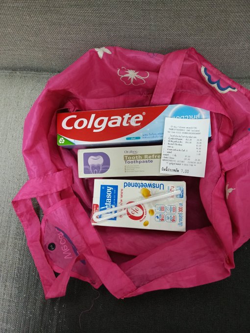 A pink tote bag contains Colgate toothpaste, Dr. John's Tooth Refresh Toothpaste, a toothbrush, and a receipt.