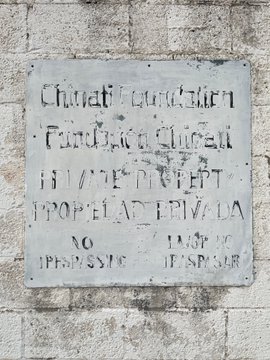A weathered stone plaque on a wall contains faded Latin-style text including 'FUNDATA QUR' and 'NO IESV ITERNI IF EROSIER'.