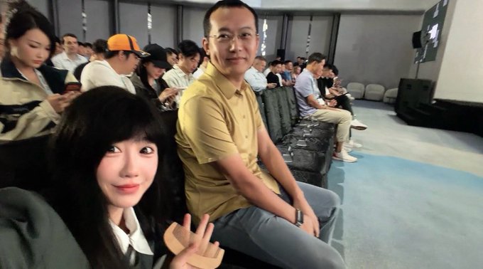 A selfie of a smiling woman with long dark hair sitting next to a man in glasses and a yellow shirt at what appears to be an event or screening.