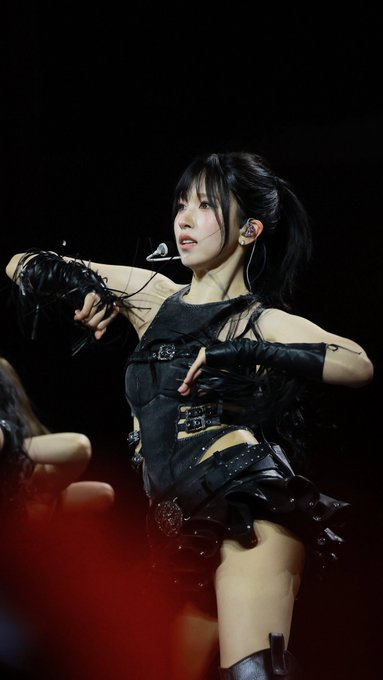 A performer in a black leather outfit with an earpiece performing on stage under dramatic red lighting.