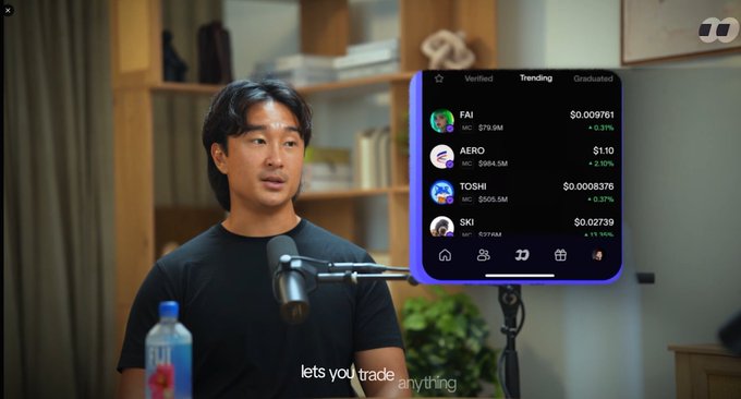 A man in a black t-shirt speaks into a microphone in a video, with a crypto trading app overlay showing trending tokens: FAI ($0.009761), AERO ($1.10), TOSHI ($0.0008376), and SKI ($0.02739).
